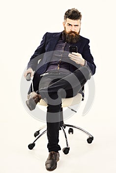 Employer holds smartphone. Director with long beard and serious face. CEO sits in office chair and looks busy. Mature