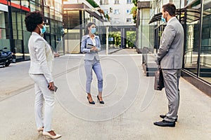 Employers standing in social distance wearing face mask looking at each other and talking