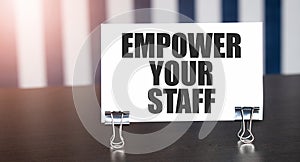 EMPOWER YOUR STAFF sign on paper on dark desk in sunlight. Blue and white background