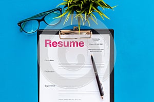 Empoyment concept with resume on blue work desk background with pen, glasses top view