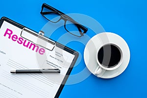 Empoyment concept. Resume on pad near pen, glasses, coffee on blue background top view