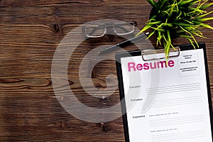 Empoyment concept with resume on wooden work desk background with pen, glasses top view space for text