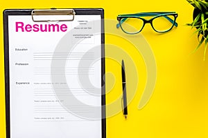 Empoyment concept with resume on yellow work desk background with pen, glasses top view