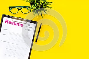 Empoyment concept with resume on yellow work desk background with pen, glasses top view space for text