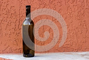 Empty 0.75 liter wine bottle against a terracotta colored concrete wall