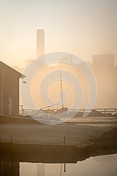 Empty abandoned sail boat club yard shrouded in fog and mist with boats sails and power station cooling tower chimneys