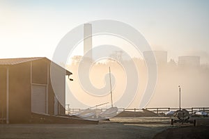 Empty abandoned sail boat club yard shrouded in fog and mist with boats sails and power station cooling tower chimneys