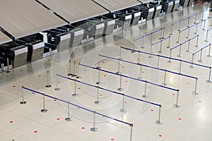 Empty airport check-in counter hall with crowd control barriers