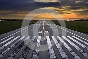 Empty airport runaway with braking and maneuvering marks, designation 29 and all navigation lights on at the colorful sunset