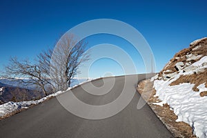 Empty alpine mountain road with snow on sides, blue sky