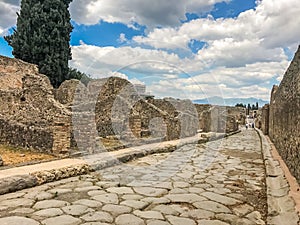 Empty Ancient Roman city of Pompeii under a blue sky with clouds. Panorama of an abandoned street in Pompeii. City ruins