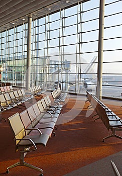 Empty armchairs in hall of expectation of airport and plane behind window