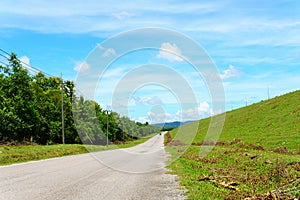 empty asphalt country road along the wall of dam with green grass and blue sky with clouds and mountain background in countryside.