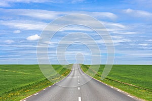 Empty asphalt country road up hill with green grass fields under white clouds and blue sky in the summer