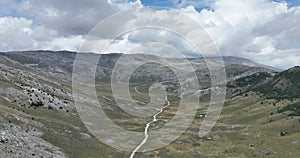 Empty asphalt road on the plateau between green fields, aerial view. Flight over long open road crossing deserted fields