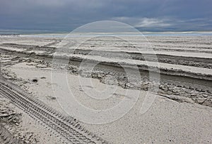 Empty baron secluded beach by the ocean with deep tire tracks in the soft sandy beach and dark storm clouds on the horizon