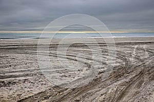 Empty baron secluded beach by the ocean with deep tire tracks in the soft sandy beach and dark storm clouds on the horizon