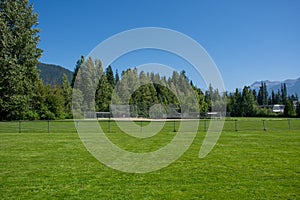 Empty baseball or softball diamond from the back fence and foul line looking towards the grass and trees in Whistler, British