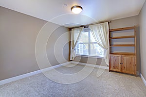Empty basement room with wooden cabinet and beige carpet.
