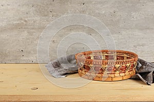 Empty basket with tablecloth on wooden table on old wall background, rustic style, eco concept, kitchen mockup for design and