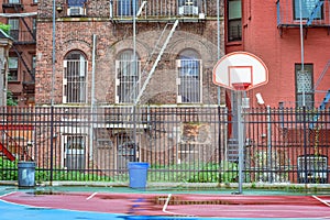 Empty basketball court on a rainy day. Surrounded by a fence and between homes. Harlem, NYC, USA