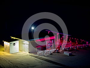 Empty beach bar with bar and chairs and tables lit with pink and white lights at night