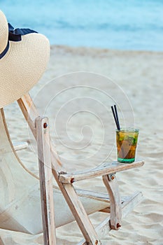 Empty beach chair on tropical summer beach with straw hat and mojito cocktail. Happy holidays summer concept