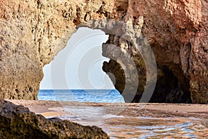 Empty beach between cliffs and natural archway through which you can see the sea. Uncrowded travel concept. Algarve, Portugal.