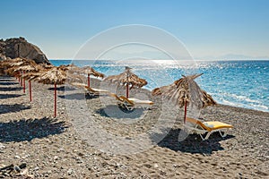 Empty beach with palm leaf umbrellas and lounge chairs on Greek island of Kos