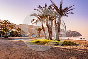 An empty beach with palm trees on an early warm and sunny summer morning as the golden sun rises over La Herradura, Costa Tropical photo