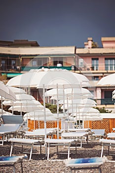 The empty beach before a rain. Mediterranean coast, empty sun beds, umbrellas from the sun, mountains, pebbles.