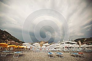 The empty beach before a rain. Mediterranean coast, empty sun beds, umbrellas from the sun, mountains, pebbles.