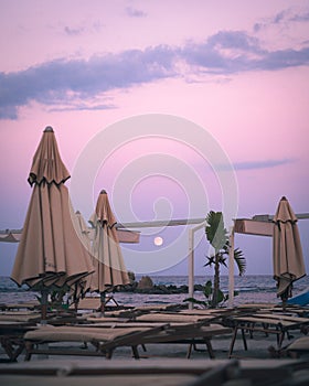 Empty beach resort at dusk with full moon under pink sky