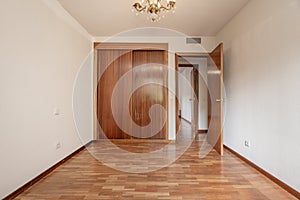 Empty bedroom with built-in wardrobe with sliding wooden doors,