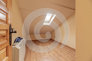 An empty bedroom with a Castilian-style paneled pine wood access door, an electric heat accumulator and sloping ceilings with