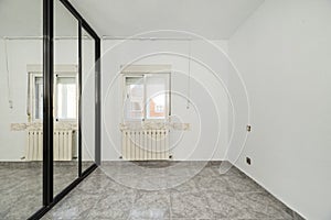 An empty bedroom with a custom built closet with black metal edged sliding mirror doors, a varnished sapele wood access door and