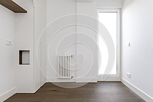 An empty bedroom with some custom-made furniture built into the wall, wooden floors and a white aluminum and glass door leading to