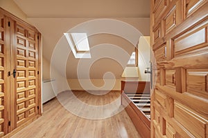 An empty bedroom with a three-section built-in wardrobe made of Castilian-style paneled pine wood, an access door made of the same