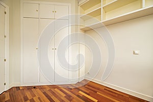 Empty bedroom with a three-section built-in wardrobe with matching trunks with white lacquered doors and matching white shelves