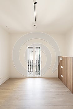 Empty bedroom with wooden headboard and white balcony windows with black wrought iron railing