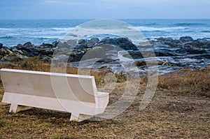 Empty bench on Atlantic Ocean coast in Portugal in the morning. Seascape in blue morning fog. Ocean beach with rocks.