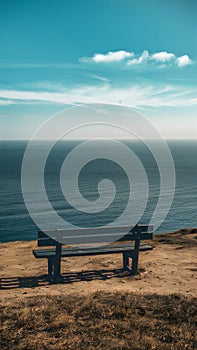 Empty bench on cliff overlooks peaceful sea, ideal for solitude