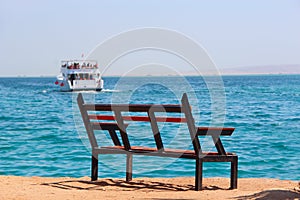 Empty bench near sea and shipped ship. Mass tourism at sea. Bench near beach
