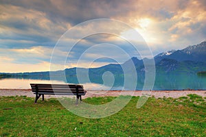 Empty bench at spring montain lake. Coast with mountains at horizon and in water mirror. Vintage toned photo.