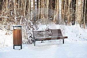 Empty bench and trash bin in snowy forest