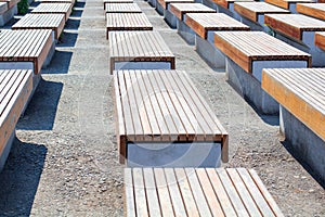 Empty benches wooden and concrete surface stand in several rows on the street in the park on the asphalt, nobody is there