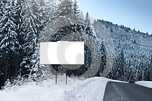 Empty billboard for advertising poster, on the background of snowy fir-trees. Winter season in a mountainous area.