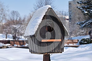 Empty bird house covered with fresh snow, on bright sunny Winter day. Close up