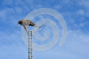 empty bird nest made with branches of trees at the top of an electrical tower of high voltage that conducts electricity to houses