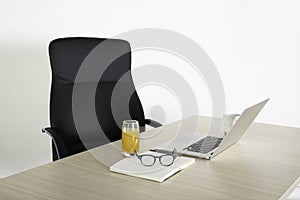 Empty black chair at a desk with a open laptop, notebook, reading glasses and glass of juice. Negative space. Copy space